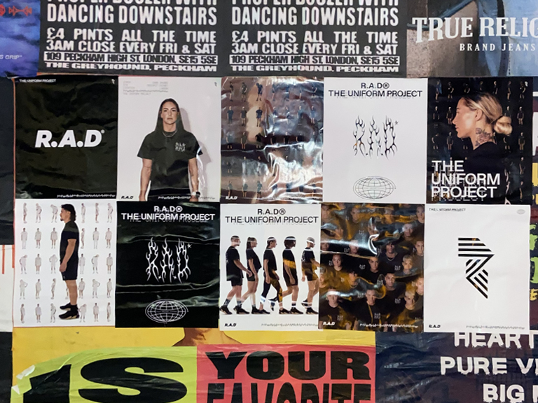 R.A.D promotional posters for "The Uniform Project" displayed on a wall, featuring diverse models and graphic designs, highlighting the campaign's visual identity in a vibrant urban setting.