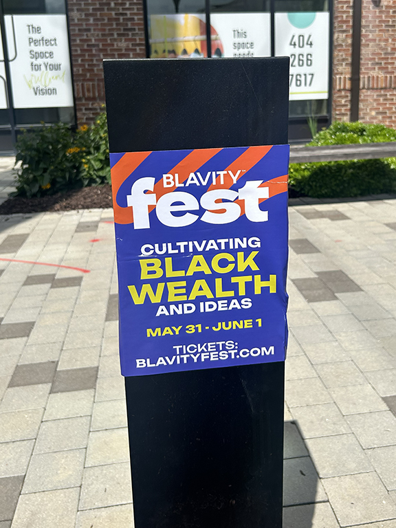 Blavity Fest promotional poster on a pole, featuring event details for "Cultivating Black Wealth & Ideas," scheduled for May 31 to June 1, with a website link for tickets.