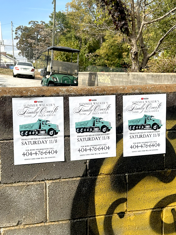 Summer Walker's "Finally Over It Dump Truck Service" promotional posters on a brick wall, featuring event details for Saturday 11/8 and contact information, with a golf cart visible in the background.