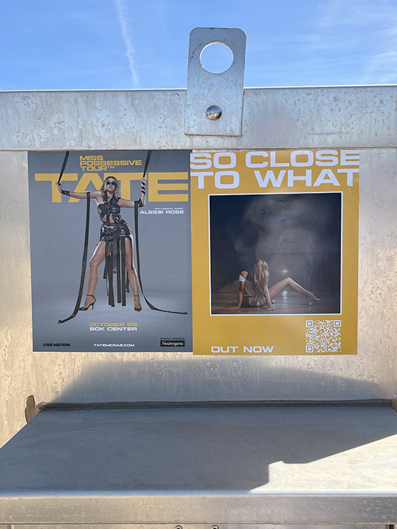 Tate McRae concert promotion poster for "Miss Possessive Tour" featuring artist image and QR code, displayed in an outdoor setting.