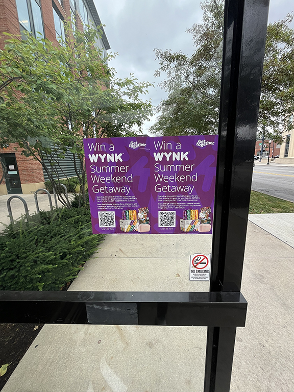 Posters promoting "Win a WYNK Summer Weekend Getaway" campaign displayed at a bus stop, featuring vibrant graphics and QR codes, relevant to Snipe Posting Activation in Columbus, Ohio.