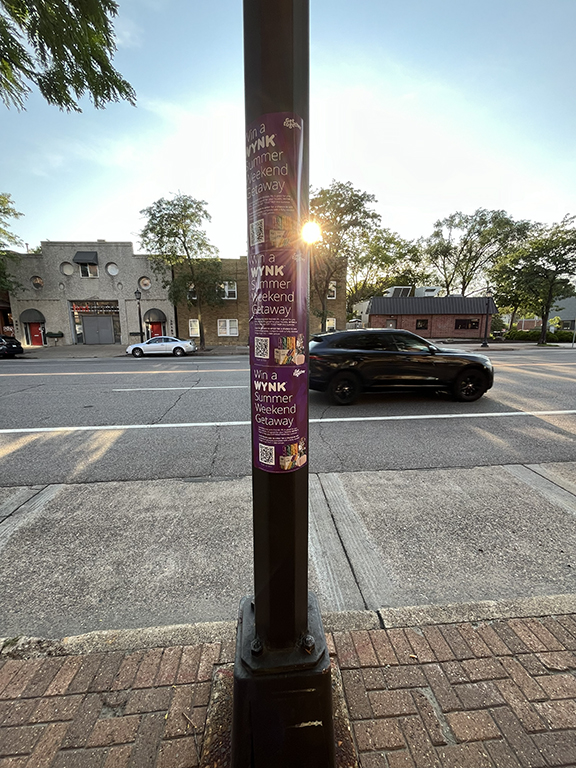 Pole advertising for WYNK's "Summer Weekend Getaway" promotion, displayed on a street light in a city setting, featuring vibrant graphics and a call to action.