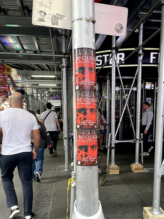 Pole displaying promotional posters for "House of McQueen," an Off-Broadway production, with pedestrians walking by in Manhattan, New York City.
