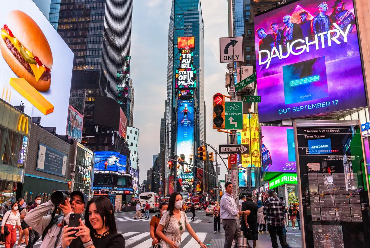 Crowd of people in Times Square, New York City, with vibrant billboards advertising Daughtry's album release and a fast-food item, showcasing the bustling atmosphere and strategic billboard placements for brand visibility.