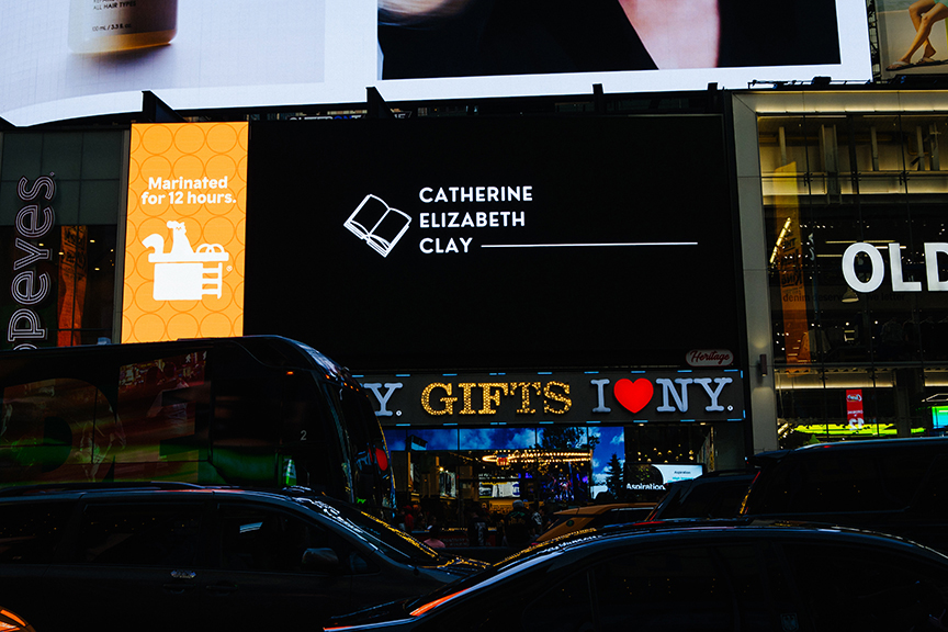 Catherine Elizabeth Clay book advertisement on a digital billboard in Times Square, New York City, alongside vibrant cityscape and traffic.