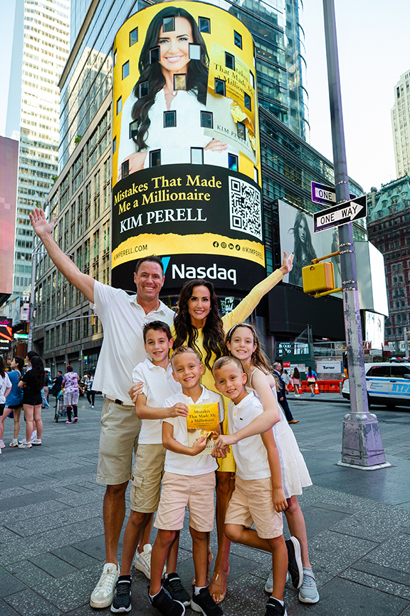 Family posing in Times Square with Kim Perell's billboard for "Mistakes That Made Me a Millionaire," featuring the Nasdaq logo and a vibrant city backdrop.