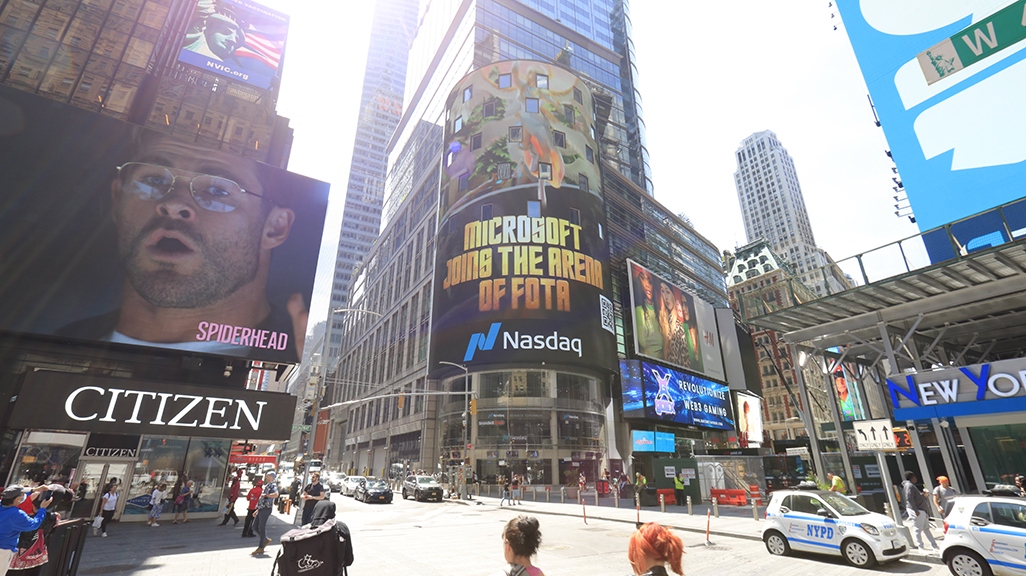 Microsoft billboard advertising "Join the Arena of FOTA" on NASDAQ Tower in Times Square, NYC, surrounded by traffic and pedestrian activity.