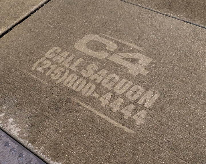 Sidewalk stencil advertising for C4 featuring the text "CALL SAQUON (215) 900-4444" imprinted on concrete, showcasing guerrilla marketing techniques.