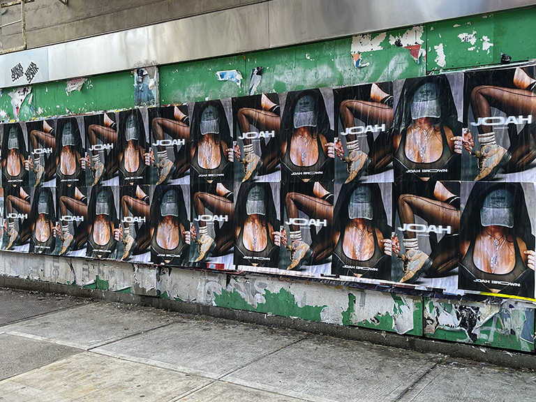Wild wheatpaste advertising campaign featuring multiple posters for Joah Brown, showcasing model in a hooded outfit against a weathered urban backdrop.
