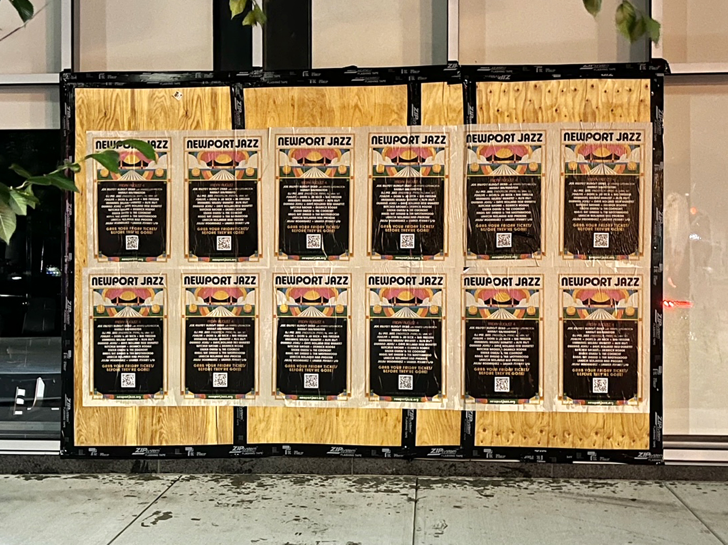 Newport Jazz Festival promotional wheatpaste posters displayed on a wooden board, featuring colorful designs and QR codes for event information.