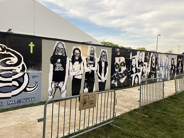 Wheatpaste mural featuring various rock band portraits and skull graphics, displayed at a festival setting, highlighting guerrilla marketing art in urban spaces.