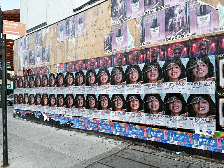 Wheatpaste poster advertisement featuring Nathy Peluso, prominently displayed on a wall, showcasing multiple images of the artist with vibrant colors and eye-catching design, relevant to urban guerrilla marketing campaigns.