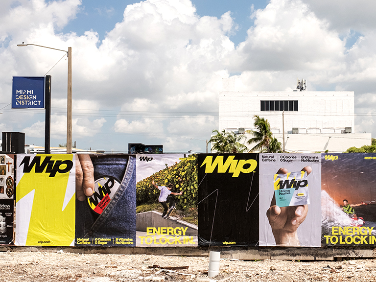 Wheatpaste advertising mural featuring vibrant graphics for WIP energy drink, showcasing various lifestyle images and product details, located in the Miami Design District, highlighting guerrilla marketing strategies.