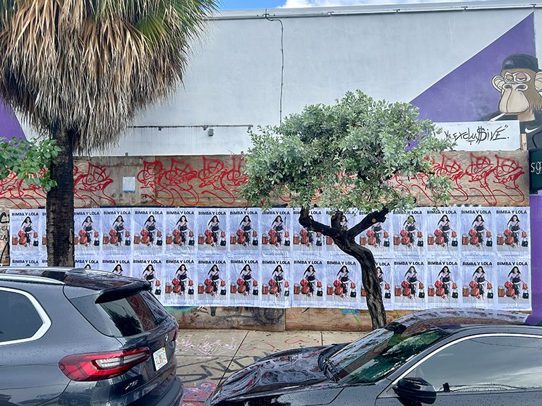 Wheatpaste advertising campaign for Bimba Y Lola on a city wall, featuring multiple posters among urban graffiti and greenery, showcasing guerrilla marketing strategies in Miami, Florida.