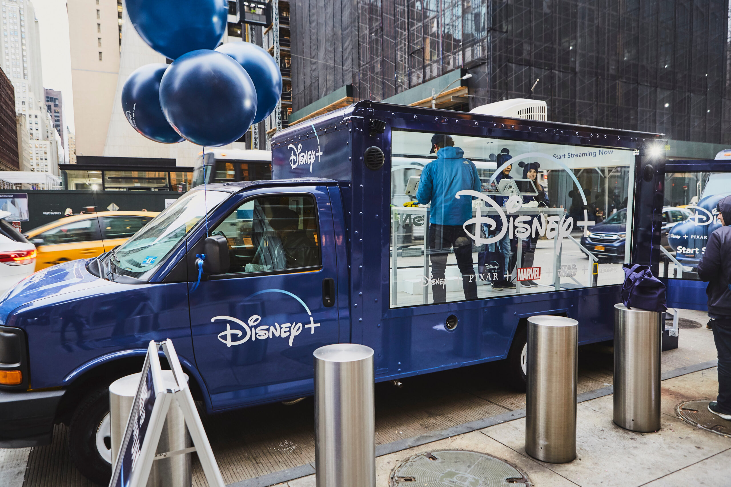 Disney+ branded mobile pop-up activation truck with promotional materials, featuring a staff member engaging with visitors in an urban setting.