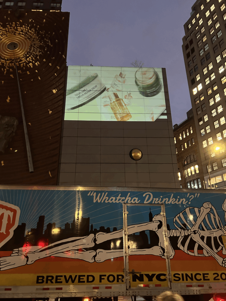 Seamless 3D LED projection of Biossance skincare products on building facade in NYC, illuminated at dusk, with vibrant visuals enhancing brand visibility.