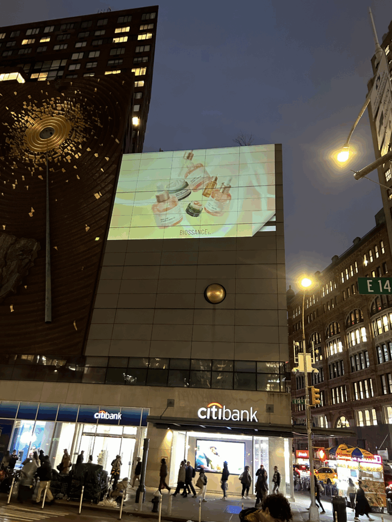 Projection of Biossance skincare products on a building facade in NYC, illuminated at night, showcasing vibrant visuals to enhance brand visibility near retail locations.