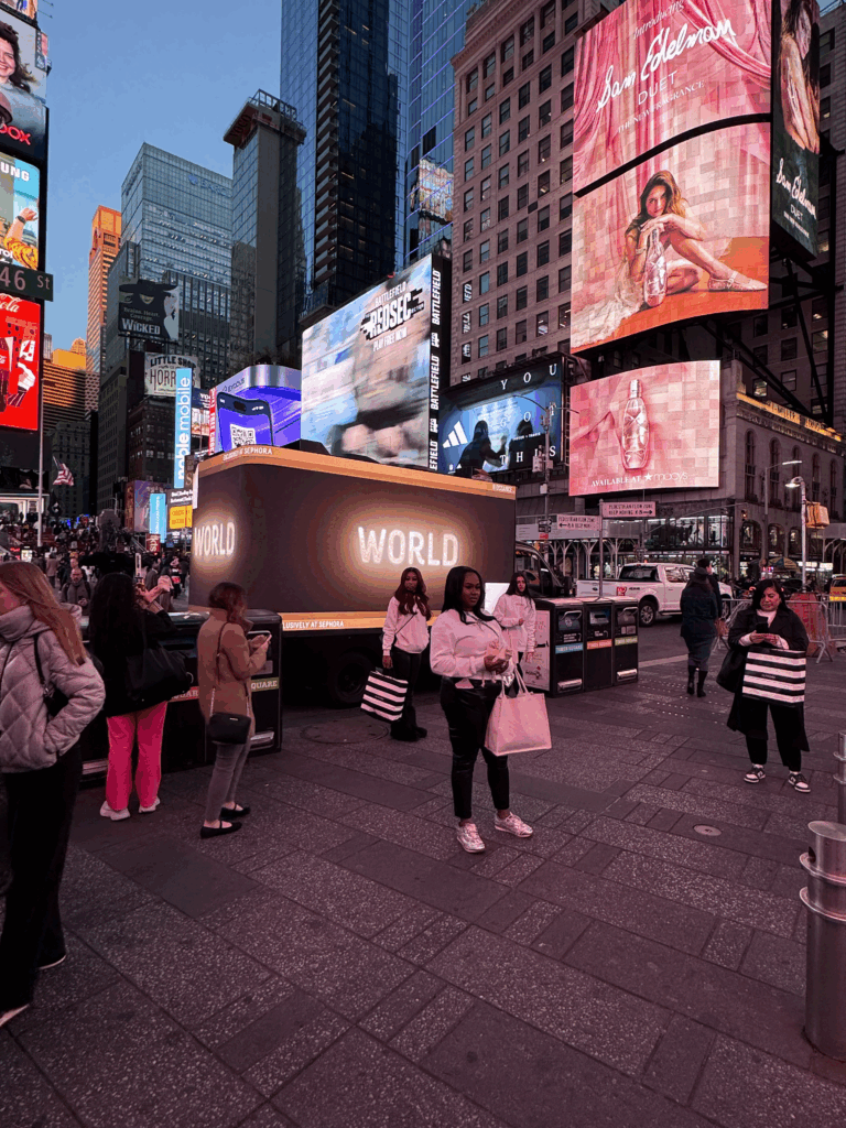 3D LED billboard truck displaying "WORLD" in Times Square, surrounded by pedestrians and vibrant advertising screens, showcasing innovative marketing for Biossance skincare products.