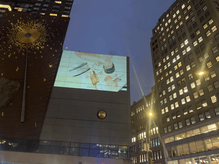 Projection of Biossance skincare product visuals on a building facade at night, surrounded by urban architecture and city lights, showcasing innovative guerrilla marketing strategy.