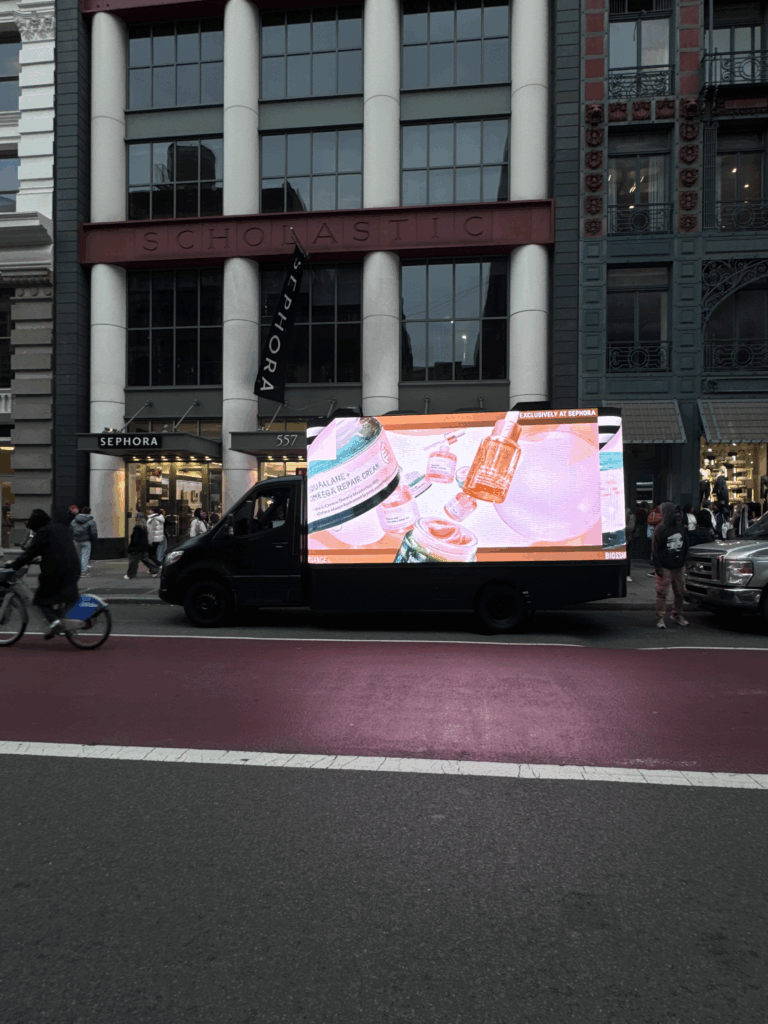 Mobile billboard displaying skincare products in front of Scholastic building, New York City, illustrating guerrilla marketing strategy by American Guerrilla Marketing.
