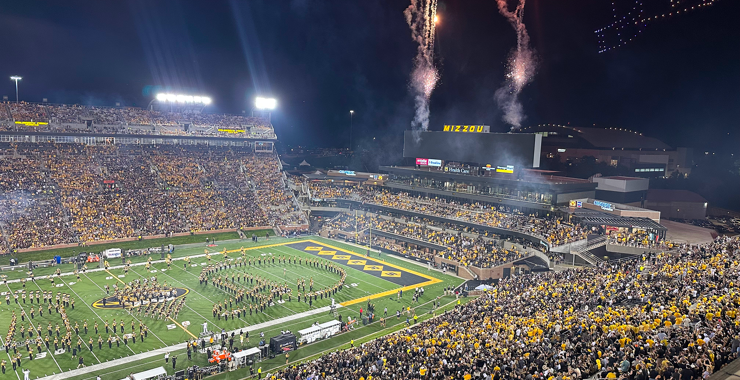 Crowd cheering at a nighttime football game with fireworks, vibrant team colors, and a lively atmosphere, showcasing a dynamic sports activation event.