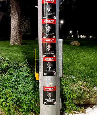 Posters with "URGENT" text displayed on a street pole, promoting brand activism and community engagement in a nighttime setting.