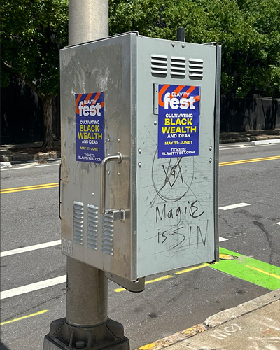 Utility box with festival posters promoting "Cultivating Black Wealth and Ideas" for a music festival, featuring graffiti stating "Magic is SIN."