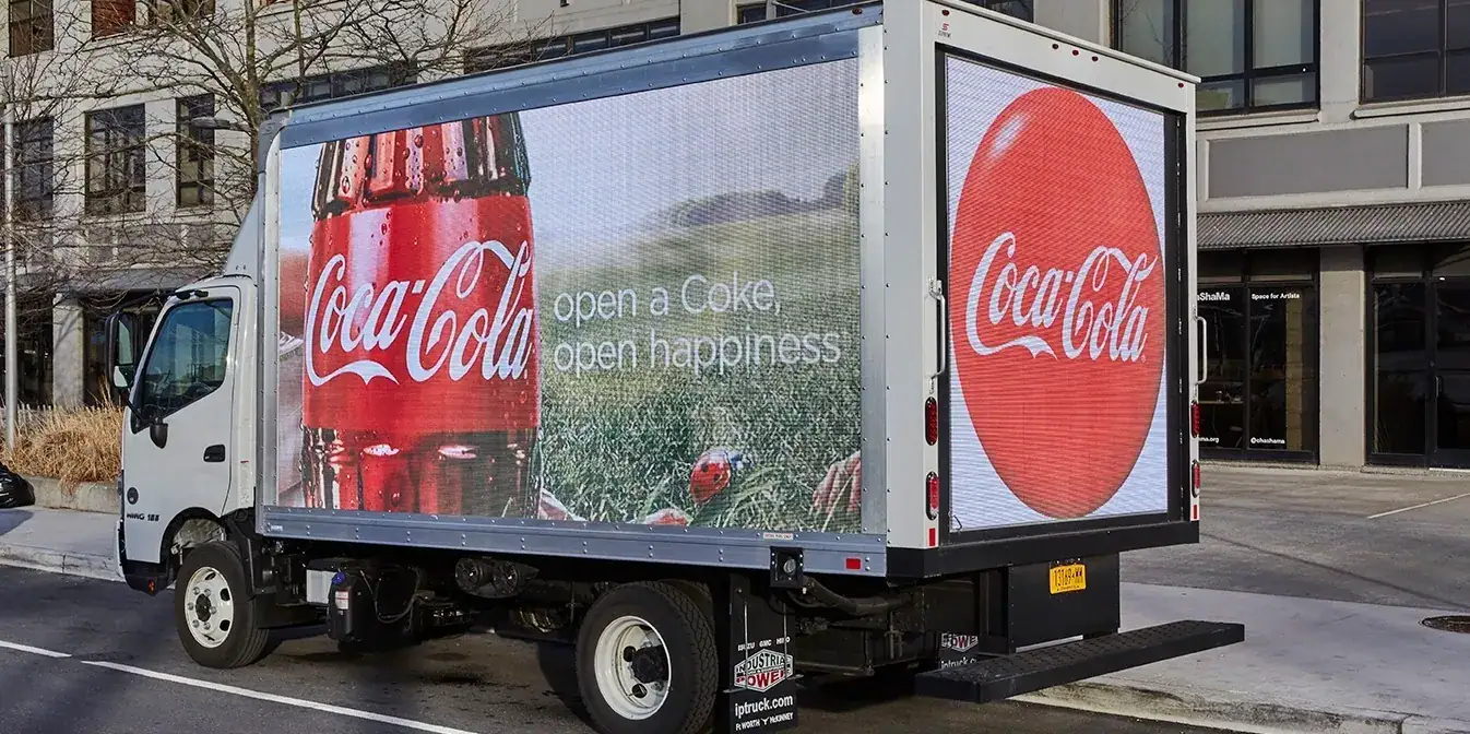 LED billboard truck displaying Coca-Cola advertisement with the slogan "open a Coke, open happiness" in an urban setting.