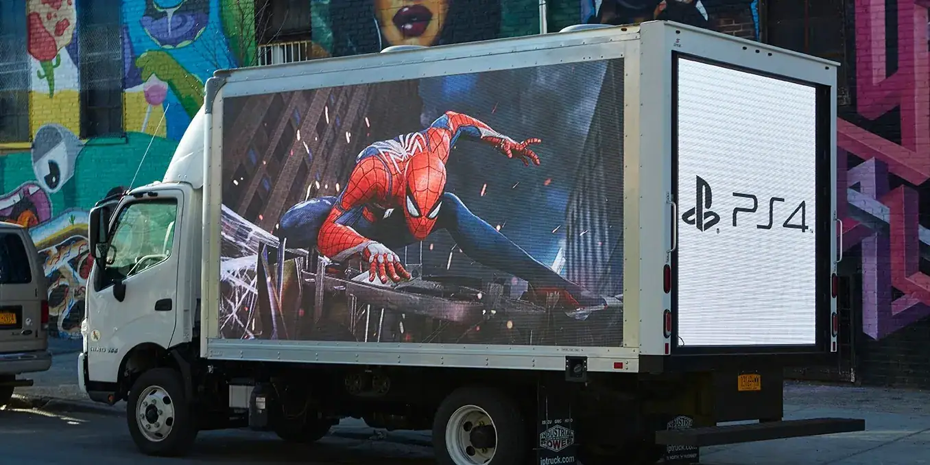 LED billboard truck displaying Spider-Man graphic and PlayStation 4 logo against vibrant urban backdrop, representing mobile advertising solutions in Texas.
