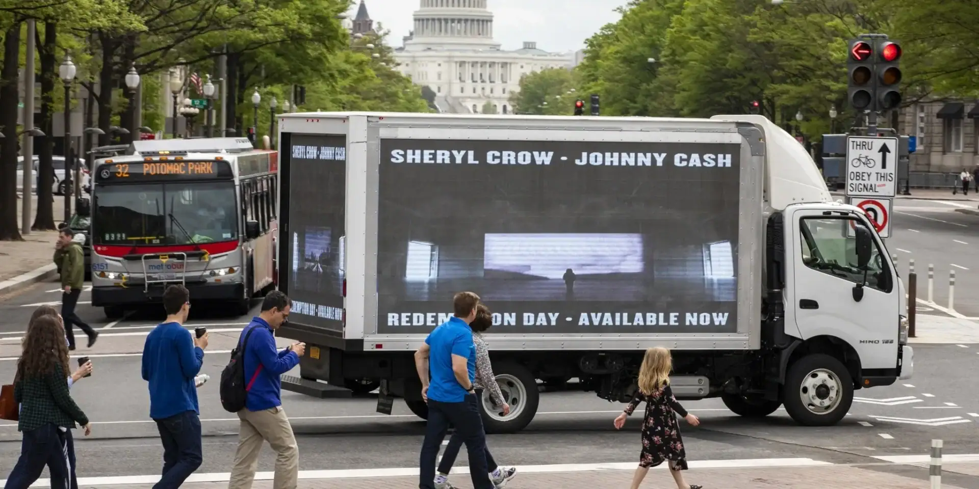 Mobile LED billboard truck displaying Sheryl Crow and Johnny Cash advertisement in Washington, D.C. street, with pedestrians and a bus in the background.