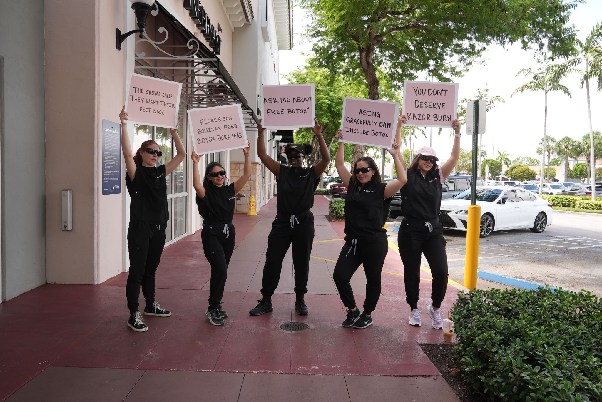 Group of street team members in black outfits holding signs promoting Botox services, engaging passersby in a lively outdoor setting.