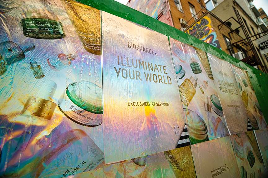 Wheatpaste poster advertising for Biossance featuring the tagline "Illuminate Your World" with product imagery, showcasing urban marketing creativity in Manhattan.