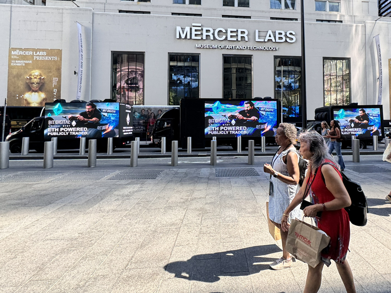 Crowd walking past Mercer Labs, featuring digital billboards promoting purpose-driven marketing campaigns and technology innovations.
