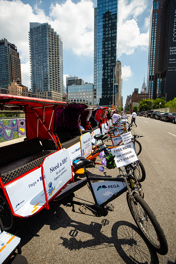 Pedicabs lined up on a city street featuring promotional signage for Pega, advertising free rides and engaging with passersby, showcasing experiential marketing and community interaction.