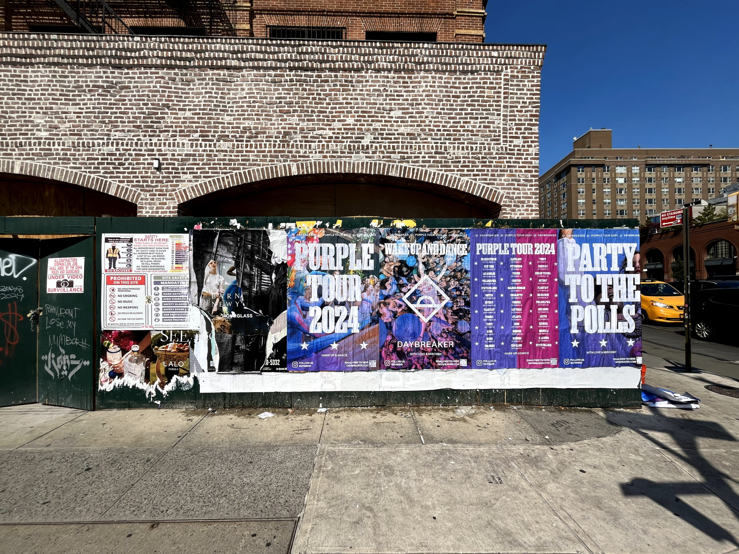 Wall covered with colorful posters promoting the "Purple Tour 2024" and "Party to the Polls," highlighting community engagement and activism through outdoor advertising in an urban setting.
