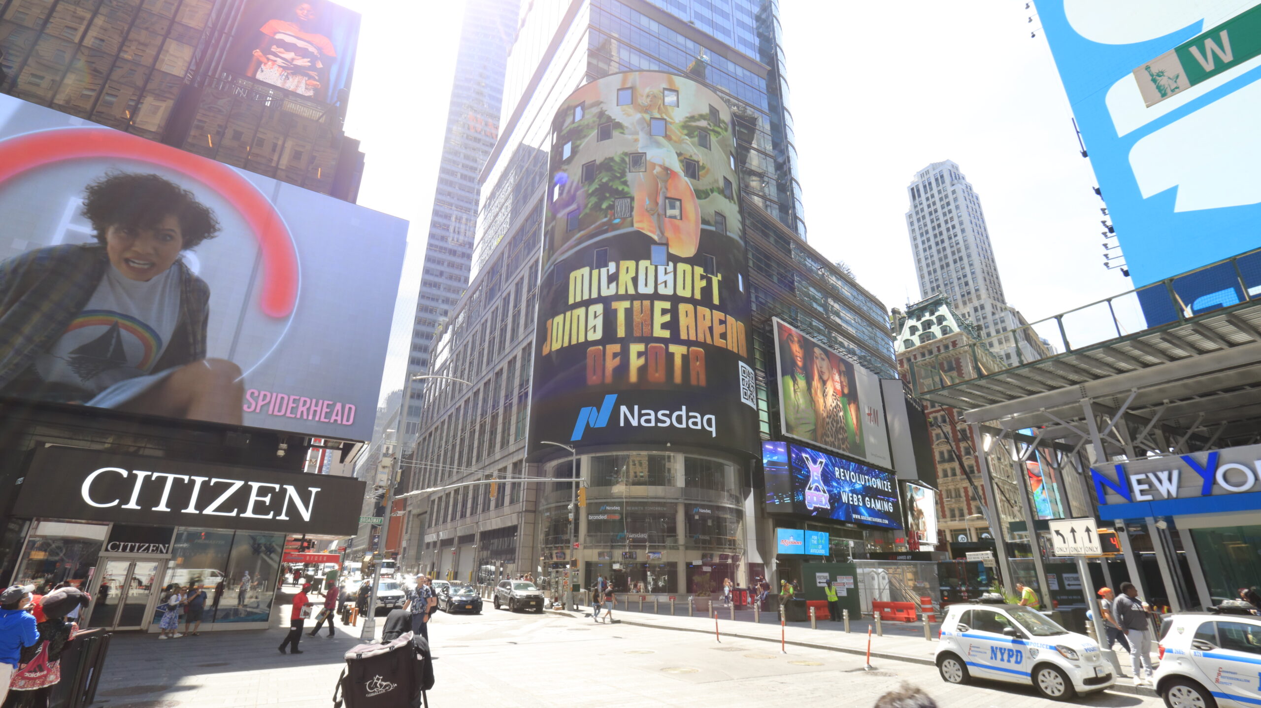 Microsoft NASDAQ billboard in Times Square, showcasing a vibrant advertisement with "MICROSOFT JOIN THE ARENA OF FOTTA" text, surrounded by bustling urban environment and other digital displays.
