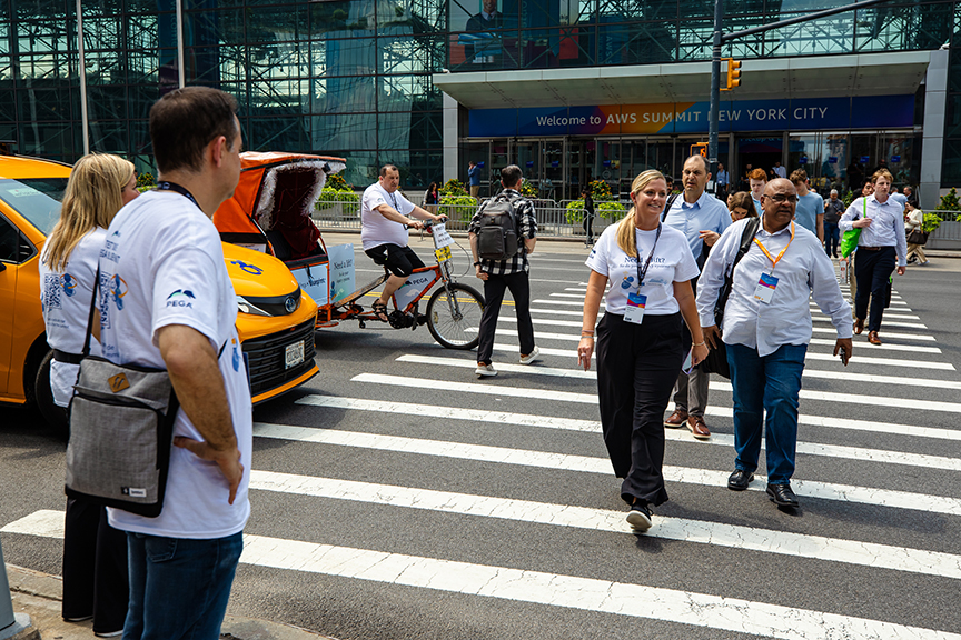 Pedicab advertising in urban setting with pedestrians and drivers in branded clothing near AWS Summit event in New York City.