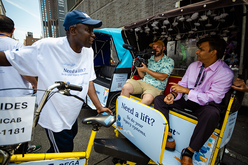 Pedicab advertising scene in NYC featuring a driver in a white shirt, a passenger in a pink shirt, and a man filming, promoting innovative guerrilla marketing services.