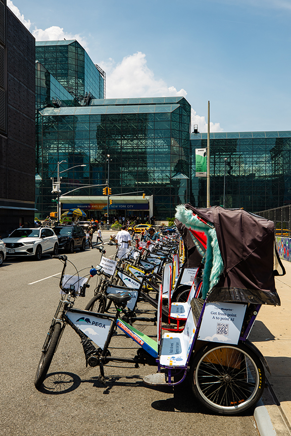 Row of colorful pedicabs parked on a city street near a modern glass building, showcasing pedicab advertising potential for urban marketing campaigns.
