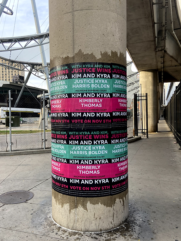 Column wrapped with vibrant campaign posters for Kim and Kyra, featuring names and slogans, promoting voter engagement for the November 5th election at a major stadium entrance.