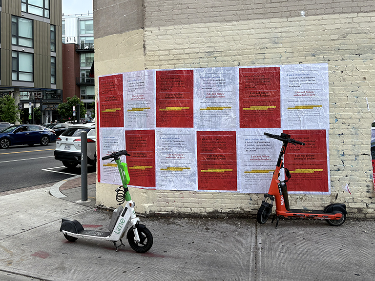 Large-scale wild posting wall featuring vibrant political campaign posters in red and white, positioned on a brick surface, with electric scooters parked nearby, emphasizing grassroots voter engagement and visibility.