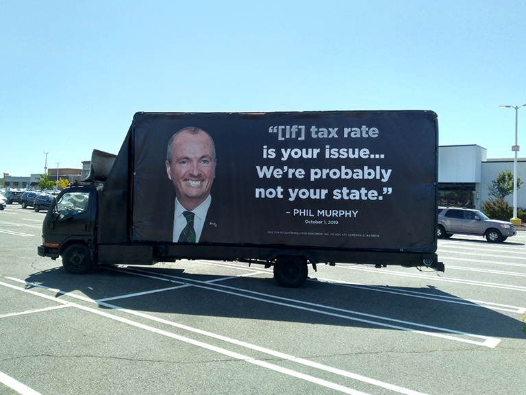 Mobile political billboard truck displaying Phil Murphy's message, featuring a large portrait and text addressing tax rates, designed for high visibility in urban settings.