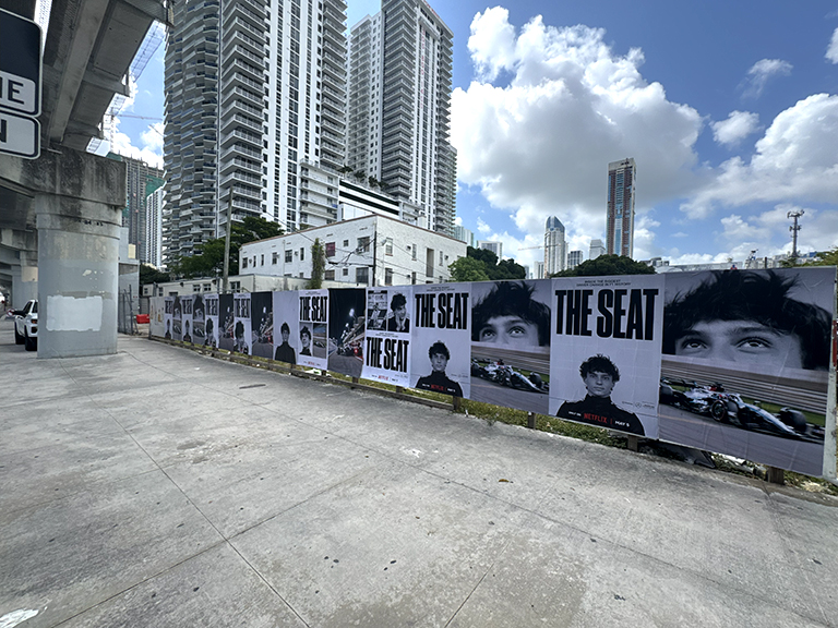 Wheatpaste posters featuring bold designs with the text "THE SEAT," displayed along a city street, surrounded by high-rise buildings and a clear blue sky, showcasing outdoor advertising strategies for impactful visibility.