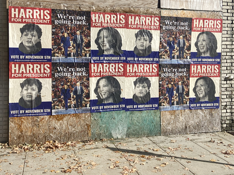 Political campaign posters for Harris, featuring diverse faces and slogans like "We're not going back" and "Vote by November 5th," displayed on a weathered wall, emphasizing grassroots political marketing strategies.
