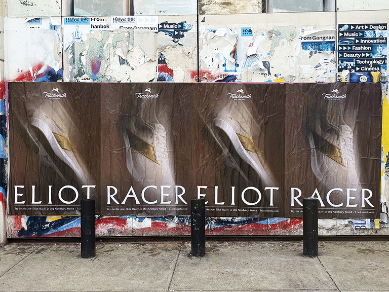 Posters advertising the "Eliot Racer" sneaker by Tracksmith, prominently displayed on a weathered wall with vibrant street art and various other posters in the background, emphasizing guerrilla marketing techniques in urban settings.