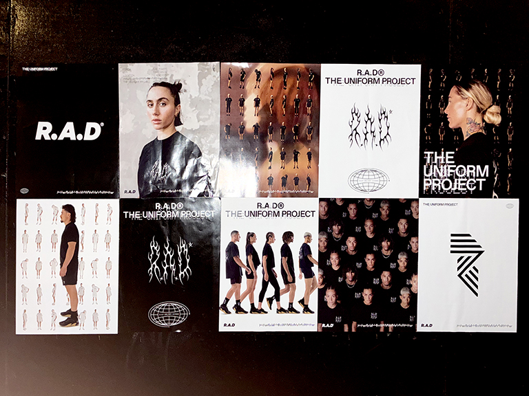 Posters featuring "R.A.D" and "The Uniform Project" displayed on a wall, showcasing various designs, including models in different outfits and artistic graphics, relevant to guerrilla marketing and street-level advertising strategies.