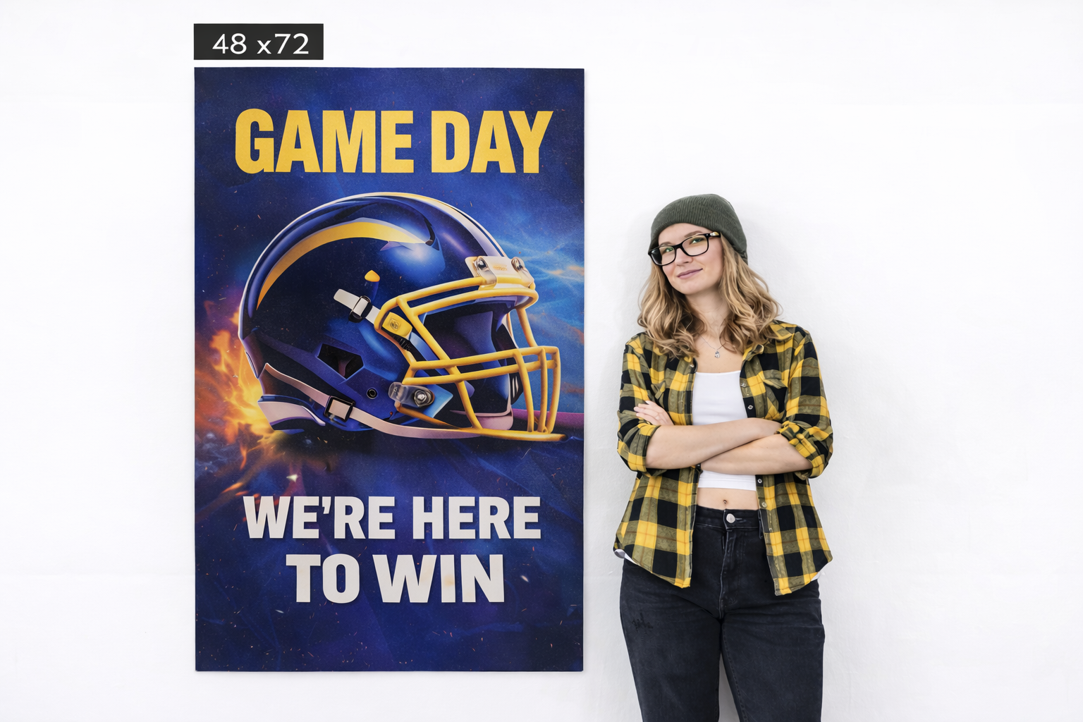 48 x 72 inch poster featuring a football helmet and bold text stating "GAME DAY WE'RE HERE TO WIN," with a woman in a yellow and black plaid shirt and glasses standing beside it, illustrating oversized poster effectiveness for high-impact marketing campaigns.